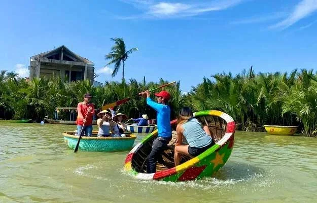 Tourists wearing conical hats riding round basket boats through a lush coconut forest in Da Nang, Vietnam.