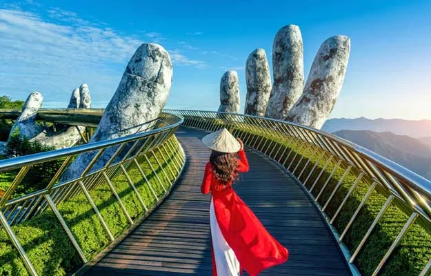 A woman is walking on the Golden Bridge held by giant stone hands in Da Nang, Vietnam